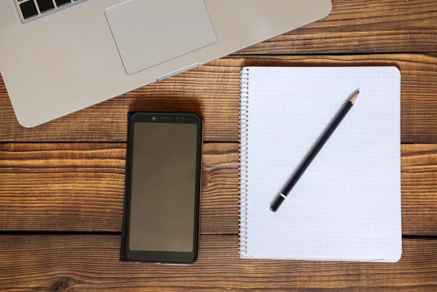 A mobile phone, notepad and pencil on a wooden desk