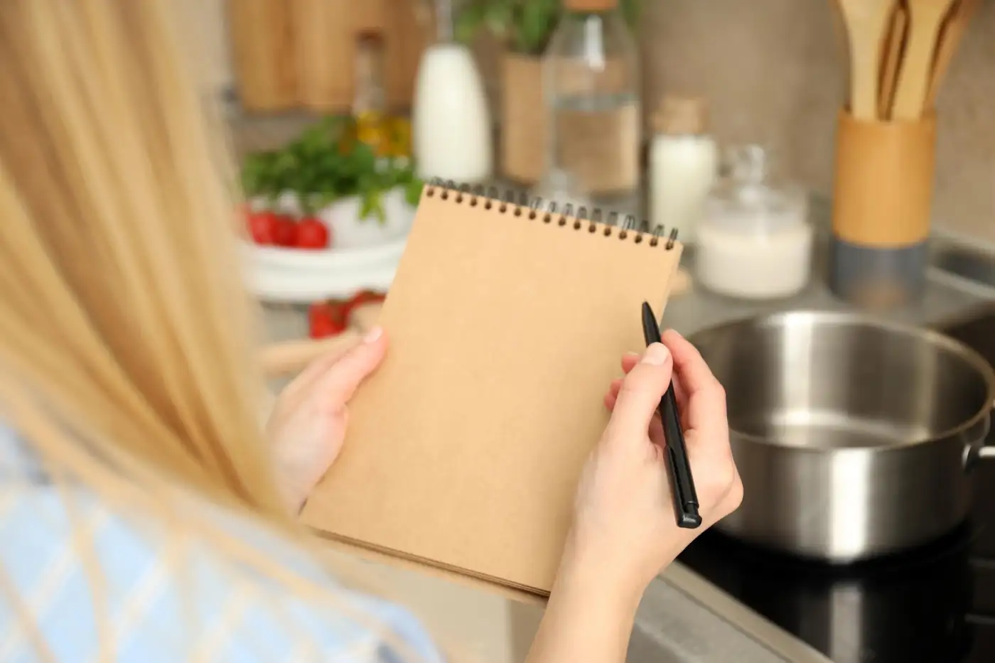 A hand writing in a notepad on a kitchen worktop