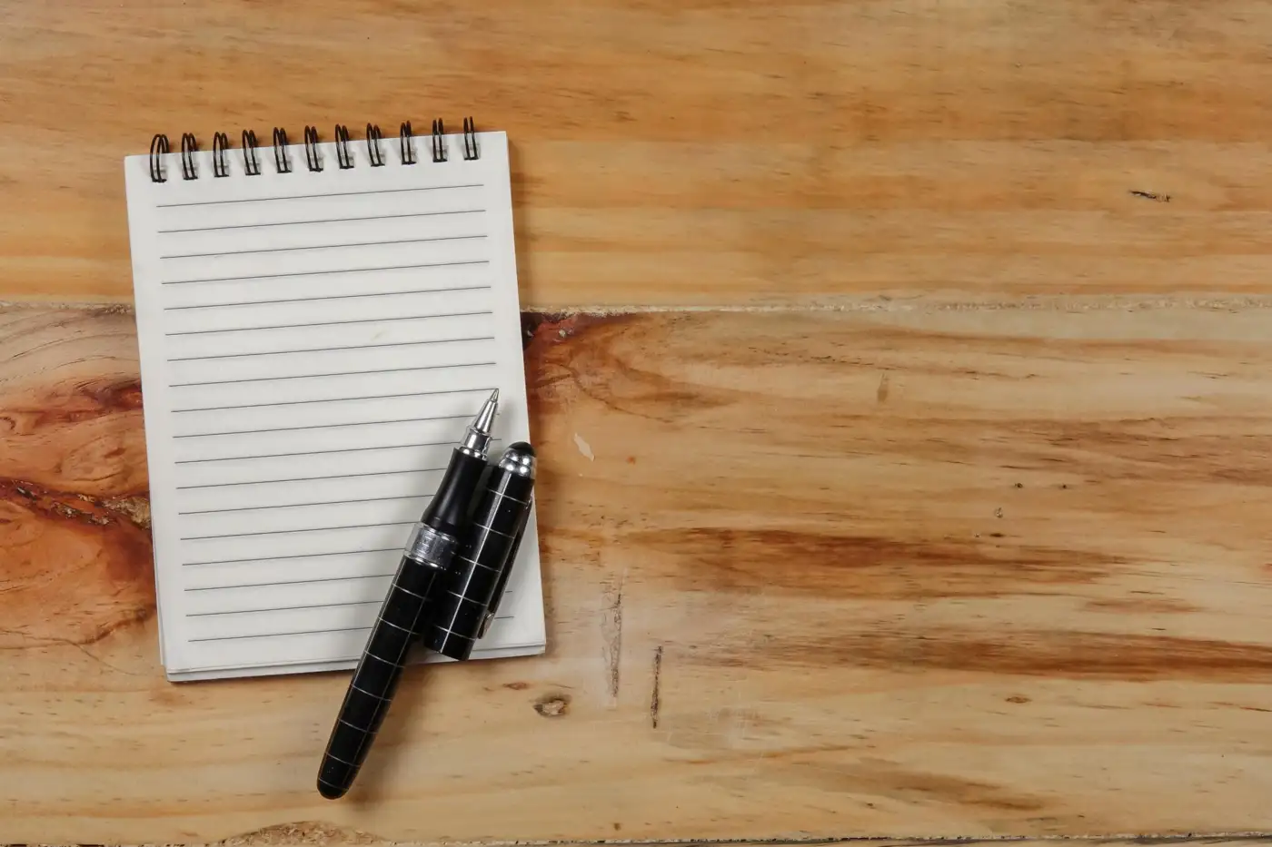 A lined notepad and a pen on a wooden table
