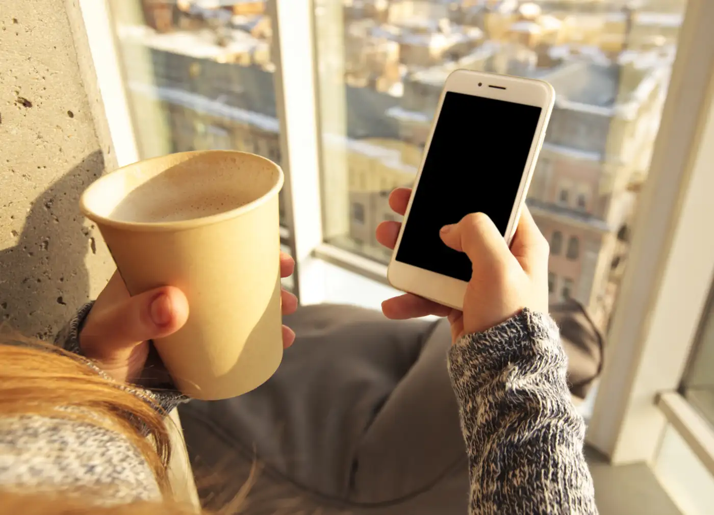 Hands holding a mobile phone by a window