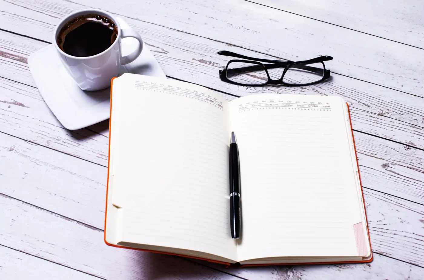 An open notebook and pen beside a cup of coffee