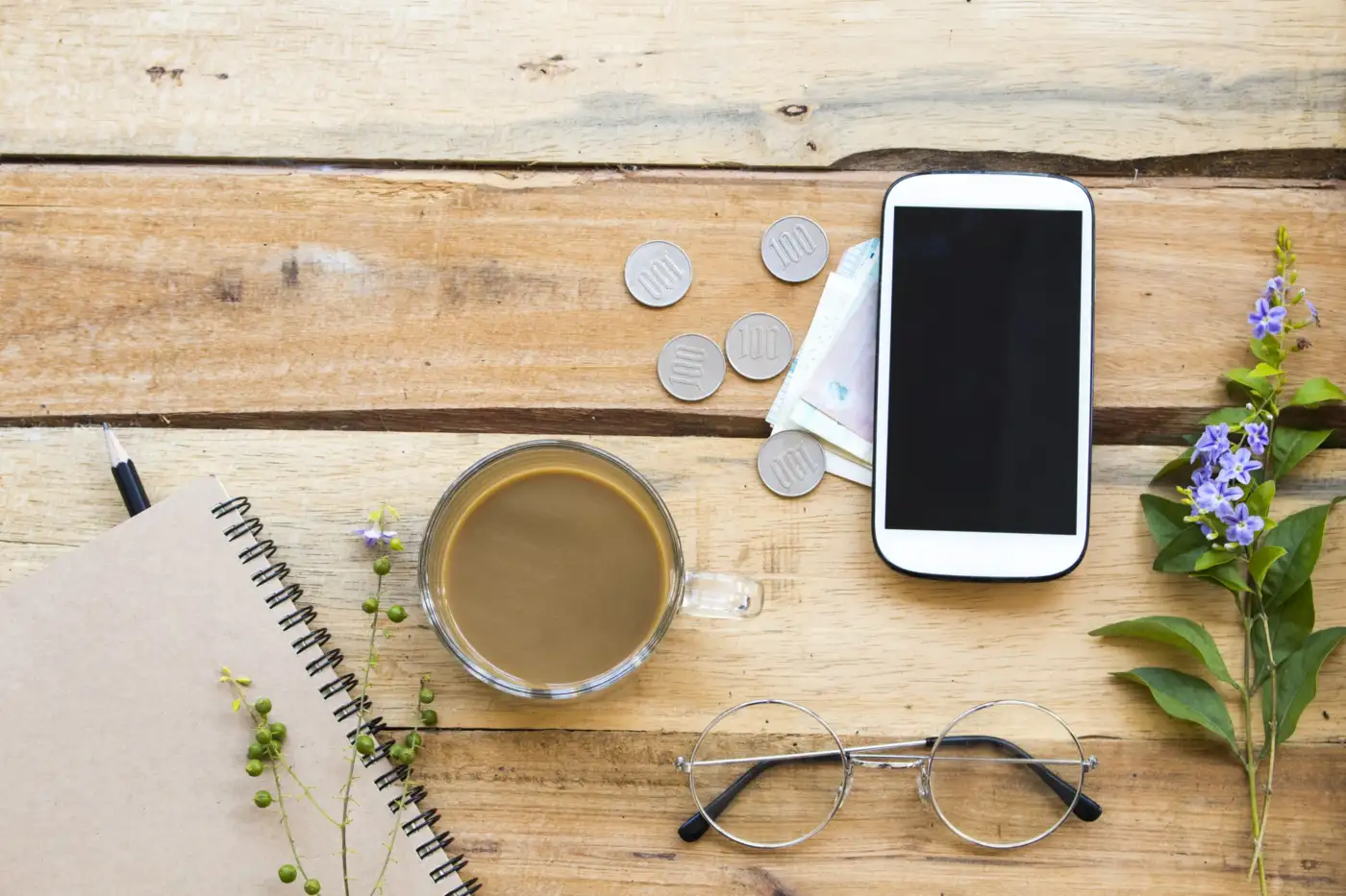 Coins, a phone and a notebook on a wooden table