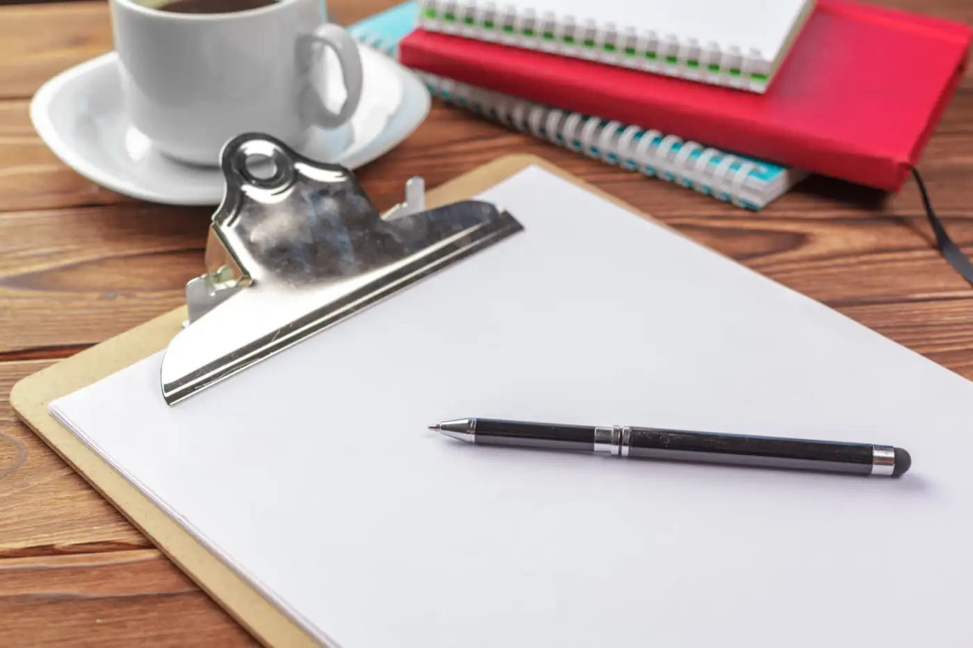 A clipboard with a blank sheet and a pen on a desk