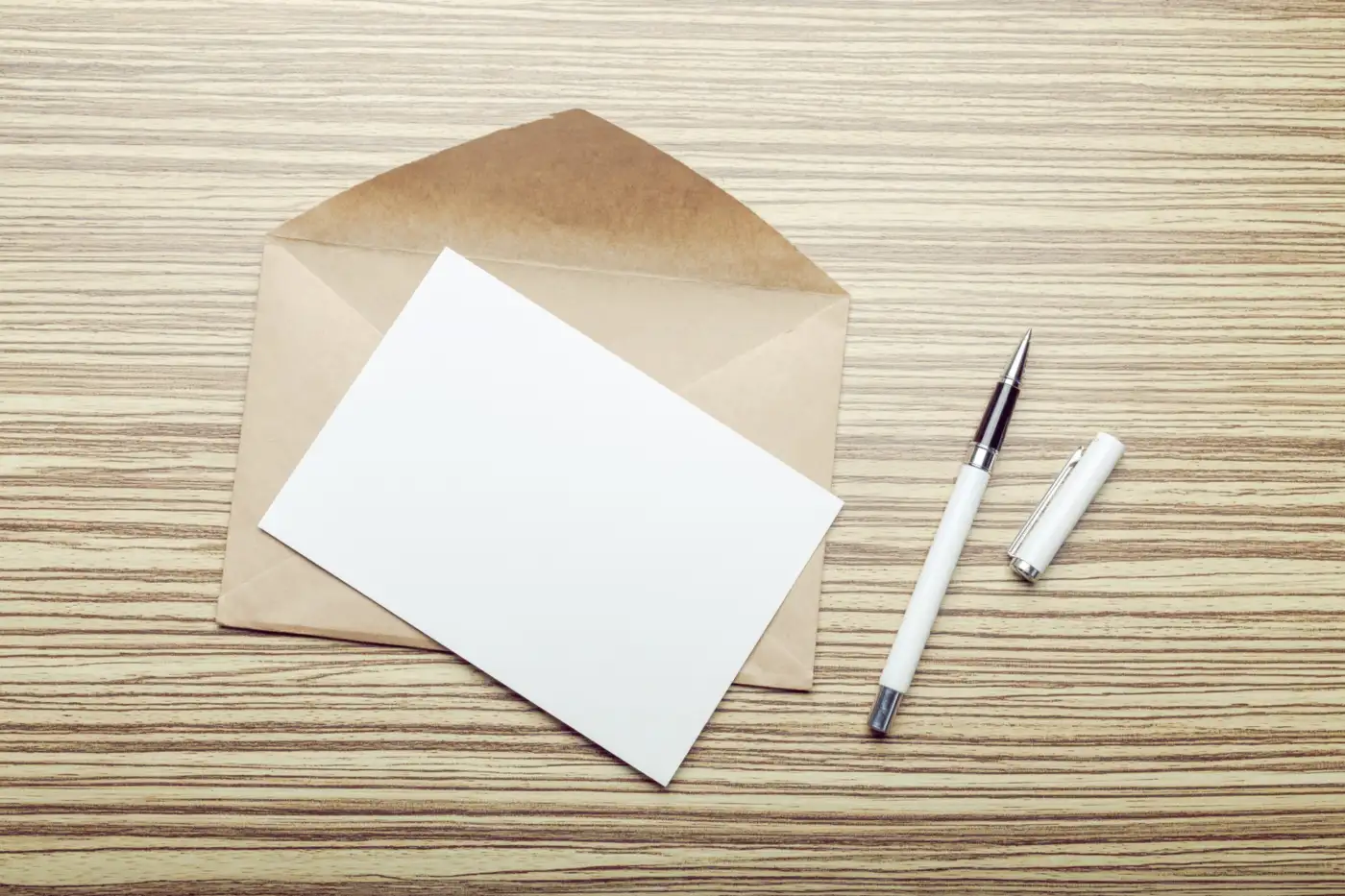 A plain envelope, a folded sheet and a pen on a wooden table